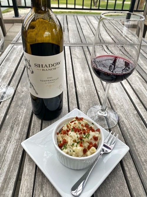 Image of a bowl of chorizo and manchego macaroni and cheese sitting on a table with a bottle of Tempranillo and glass of red wine behind it 